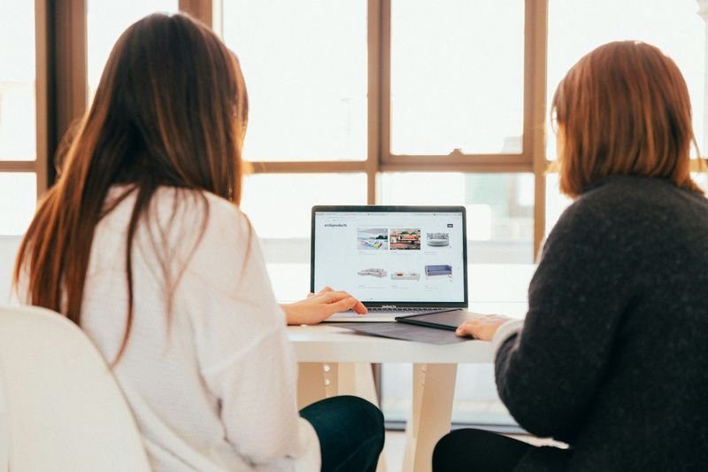 Two people sitting at a table in natural light, looking together at a laptop screen as they talk through options