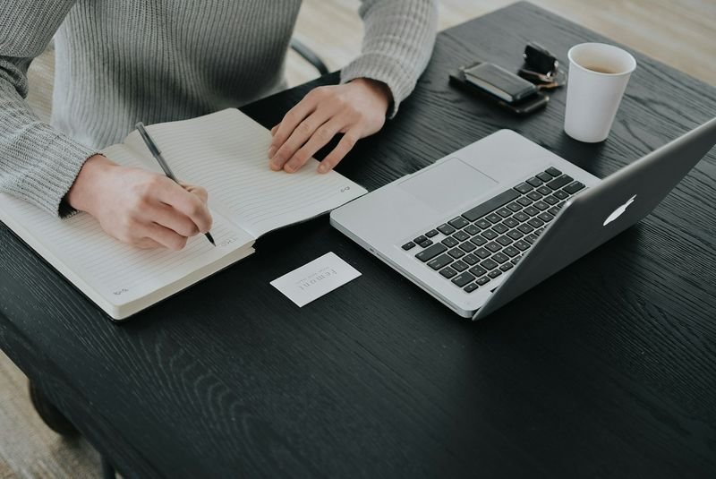 A notebook and pen next to an open laptop on a desk, set up for planning a decision
